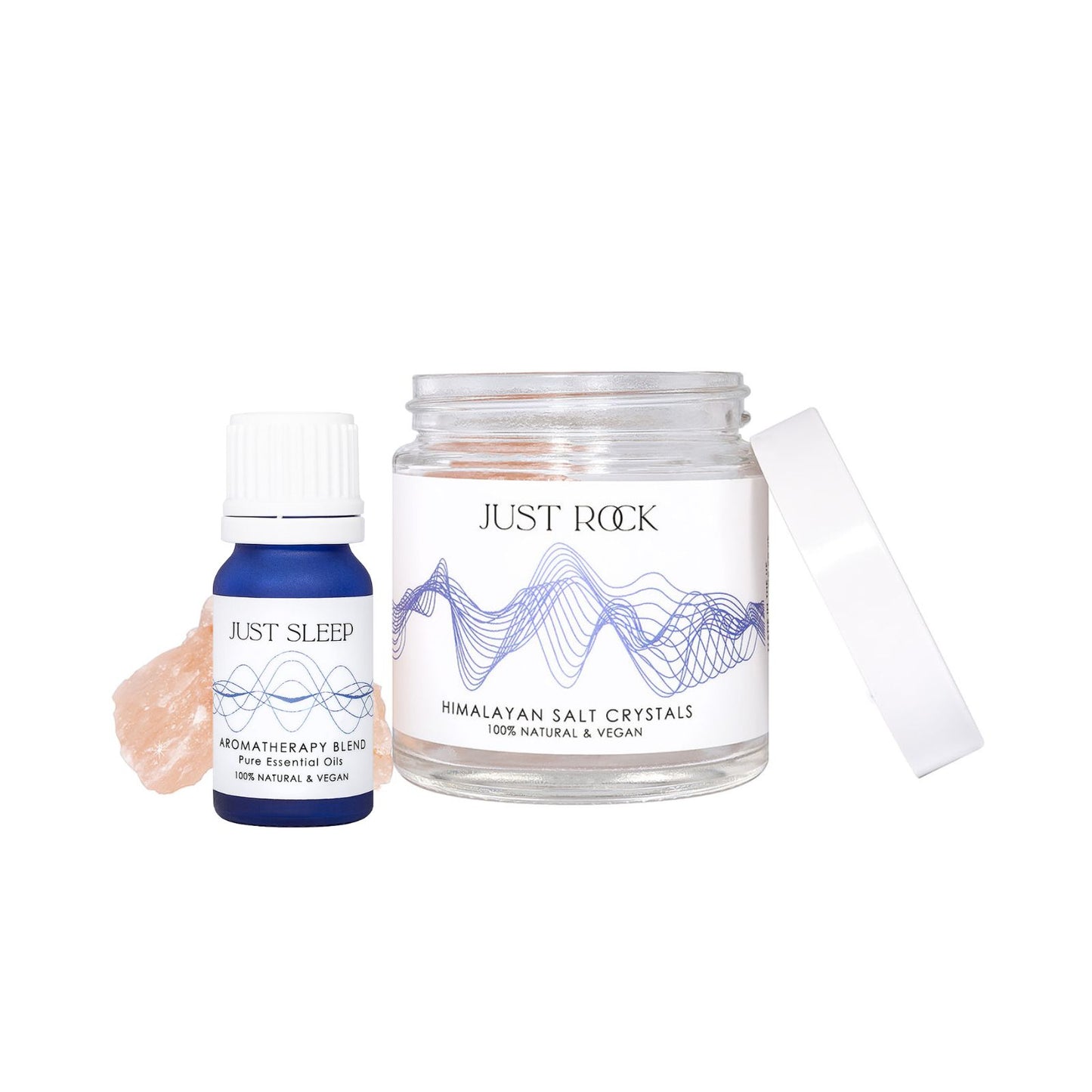 A small blue glass bottle with text JUST SLEEP - Aromatherapy Blend - pure essential oils stands next to a clear glass jar with text JUST ROCK - Himalayan Salt Crystals. Visible in the jar and next to the bottles are pink salt rocks